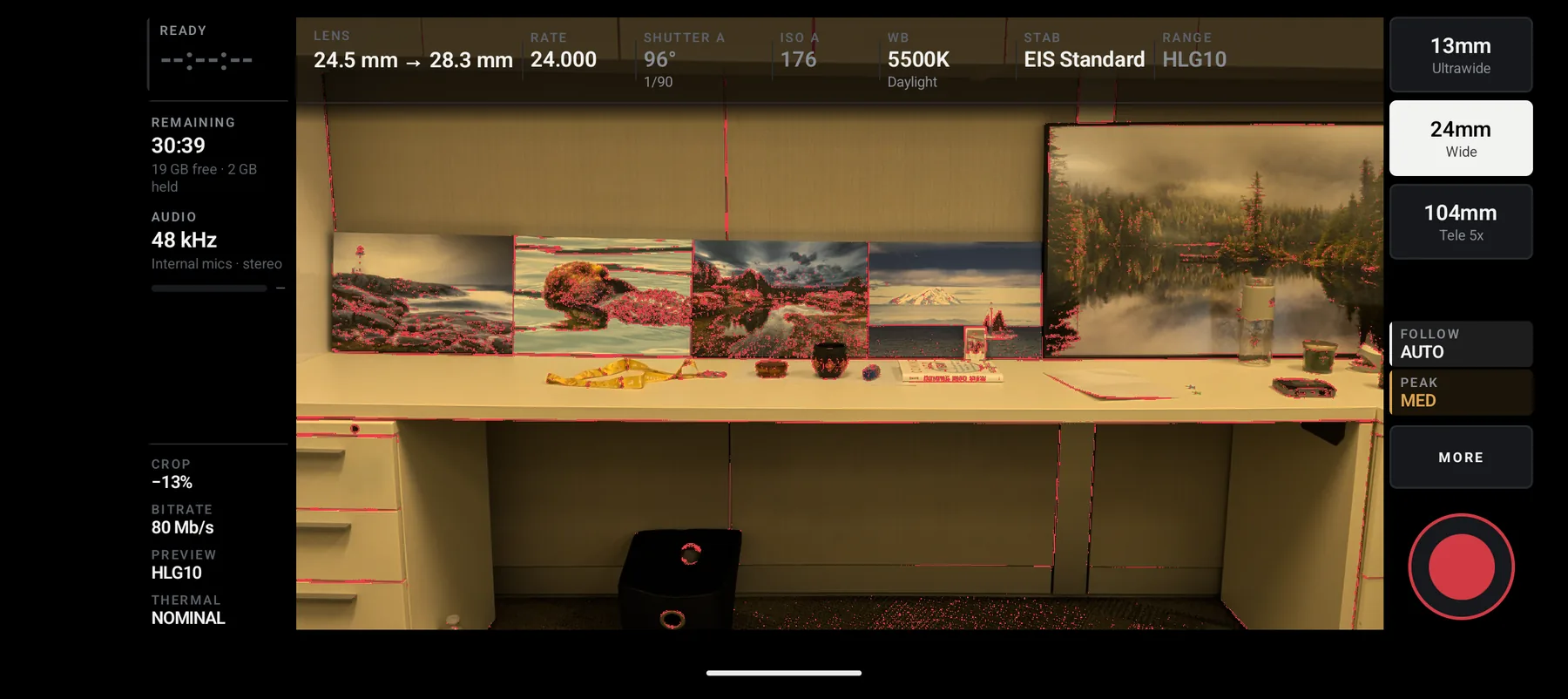 The same scene with focus peaking on: red speckle over the in-focus edges of
                  the framed prints and the desk, and the rail button reading PEAK MED.